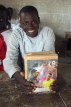 Tanji village.  Smiling student from Usman Bun Afan private Islamic school proudly showing his exercise book with picture of a football referee showing a yellow card to Brazilian football player Cafu....