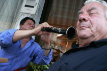 Toumba.  Street musician playing clarinet  perspective and angle of picture giving appearance that he is directing instrument and sound towards ear of elderly man in foreground. artistfacial express...