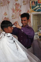 Young Indian barber in his barbershop cutting the hair of a boy.fashionhaircutinteriorjobworkinghair stylecreativitystylingstyleAsia Asian Bharat Immature Inde Intiya Rajasthani