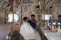 Young Indian barber in his barbershop cutting a boys hair.haircutinteriorjobworkinghair stylestylingstyleAsia Asian Bharat Immature Inde Intiya Rajasthani