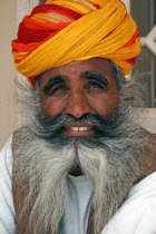 Meherangarh Fort.  Head and shoulders portrait of a smiling Indian man with long  grey beard wearing red  yellow and orange turban.racecolourscolorsexpressioncharacter Asia Asian Bharat Gray Happ...