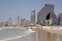 Beach with people sunbathing and at waters edge overlooked by high rise  modern city buildings reflected on wet sand.seasummesunvacationholidayBeaches Isra el Israeli Middle East Resort Sandy Se...
