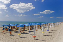Lines of coloured sun umbrellas and striped deck-chairs along quiet stretch of beach overlooking sea.  Blue sky and white clouds above. summerhotheatsandvacationholidaycalmmorningtourismGulf...