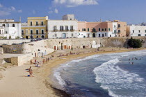 View of old city with traditional houses beside sea wall overlooking curving sandy beach with people sunbathing and swimmingApuliaGalipoliGallipolliKallipoli  Kalipolikallipolliseasunswimmers...
