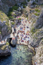 Tricase.  Looking down on people sunbathing on coloured beach towels laid out on rocks next to the sea with others in the water.  Steps leading down behind and cliff path at side.ApuliasunSummerho...