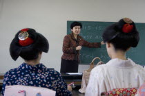 Gion area the neighbourhood where Geisha live  study and perform.  Two Geisha wearing kimono and wigs attend an English class at Mia Garatso school for Geisha  seated with backs to camera looking towr...