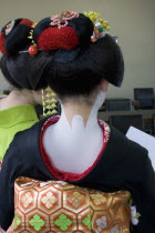 Gion District.  Back of Geisha attending a class at Mia Garatso school for Geisha wearing black silk kimono with gold and green obi.  Hair is worn up and fixed with decorative pins and flowers exposin...