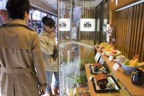 Asakusa.  Young Japanese couple standing outside a restaurant looking at the plastic food representing the menu displayed in the windowmodern lifeculturelifestyleselectionselectdecisiondecidec...