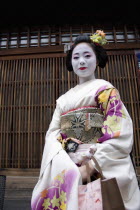 Gion District  the neighbourhood where Geisha live and perform.  Three-quarter portrait of smiling Maiko  or apprentice Geisha with hair pinned up with decorative ornaments  white facial make up  red...
