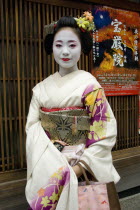 Gion District.  Three-quarter standing portrait of Geisha with white facial make up and red painted lips  hair worn up with decorative pins and wearing flower patterned  pale silk kimono.Geikotradi...