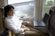 Shinkansen train series 700 known as the  bullet train .  Young Japanese man using his laptop with a wireless connection while travelling between Tokyo and Kyoto.modernrailwayspeedcomfortlifestyl...