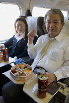 Shinkansen train series 700 known as the  bullet train .  Japanese couple eating from bento lunchbox using chopsticks while travelling between Tokyo and Kyoto.modernrailwayspeedcomfortbusinesstr...