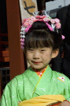 Asakusa Kannon or Senso-ji Temple.  Head and shoulders portrait of young Japanese girl wearing pink flower decoration in her hair and green kimono.ShintotraditioncultureJapanesehairstylefemaleF...
