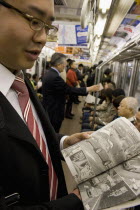 Young Japanese man wearing a suit showing the Manga comic he is reading to the photographer while travelling on the Tokyo Metro.transportationvehicleundergroundpassengerstrainrailwayanimationi...