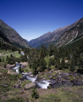 Vallee du Lutour.  View north showing  u  shape of eroded glacial valley walls.  Fast flowing river running alongside mountain path with trees on lower slopes.
