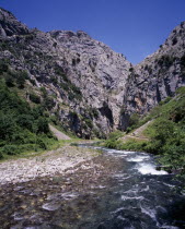 Garganta del Cares.  Rio Cares flowing towards gorge from the south.  Shallow  fast flowing water over rocks with steep eroded limestone cliffs beyond.
