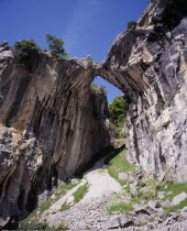 Garganta del Cares.  Water eroded roofless cave in limestone cliffs framing mountain pathway and view along gorge.