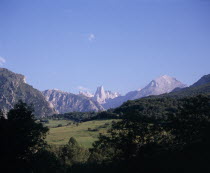 Urrieles mountain group or Central Massif with central rock pillar of Picu Urrielu 2519 m / 8252 ft seen from the north.  Pasture land and trees in central foreground.