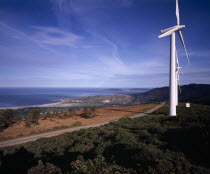 Coastal landscape with line of wind powered electricity generators and high windswept clouds.