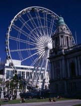 People sitting or lying in the sun in the grounds of City Hall with The Wheel of Belfast part seen behind.ferris wheel Bal Feirste Eire European Irish Northern Europe Republic Ireland Poblacht na h...