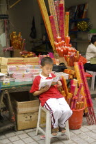 Boy incense seller reading book outside the Arhat Temple in downtown ChongqingAsia Asian Chinese Chungkuo Jhonggu Zhonggu Kids One individual Solo Lone Solitary Religious