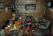 Titus and Nathaniel Moser sitting with children watching television in Rosa s house inside a Guayaquil slum. Framed painting of The Last Supper hanging on wall above the children.American Equador His...