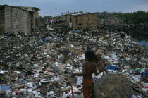 The city rubbish tip in barrio Guayas slum neigbourhood with children playing near large rock in the foreground.American Equador Hispanic Kids Latin America Latino Neighbourhood District shanty South...