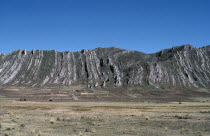Vertically folded rock strata behind agricultural land with people and cattle on the groundAmerican Bolivian Cow  Bovine Bos Taurus Livestock Farming Agraian Agricultural Growing Husbandry  Land Prod...