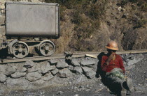 Miner wearing orange hard hat sitting next to mining rail track chewing leaves of cocaAmerican Bolivian Hispanic Latin America Latino One individual Solo Lone Solitary South America