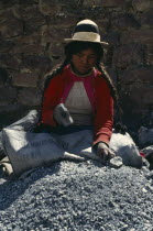 Woman sitting in a Banco Minero de Bolivia sack breaking rocks into small pieces with a hammer at a mine. Near Sucre American Bolivian Chuquisaca Female Women Girl Lady Hispanic Latin America Latino...