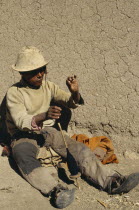 Aymara man sitting against a wall with a spindle of thread. Near SucreAmerican Bolivian Chuquisaca Hispanic Latin America Latino Male Men Guy One individual Solo Lone Solitary South America