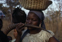 Yau woman blowing a water buck horn while carrying a load on her head standing in the fieldsAfrican Eastern Africa Female Women Girl Lady Indigenous Malawian