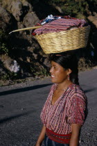 Indian girl walking along road carrying a basket of washing on top of her head with a Roman Catholic candle. Near Lake AtitlanAmerican Central America Christian Clean Cleaning Hispanic Latin America...