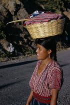 Indian girl walking along road carrying a basket of washing on top of her head with a Roman Catholic candle. Near Lake AtitlanAmerican Central America Christian Clean Cleaning Hispanic Latin America...