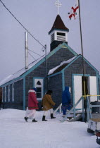 The Great Whale settlement. Cree Indigenous community. Anglican Mission Church with three women walking up the steps through the snow towards main entrance. Great Whale River Crees3 American Canadi...