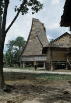 Montagnard village. Woman walking along path near buildings built on stilts  one with a steep thatched roof Kon TumAsian Southeast Asia Viet Nam Vietnamese 1 Female Women Girl Lady One individual So...