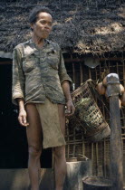 Vietnam War. Man standing next to thatched roof hut at Dak Pek United States and Montagnard Special Forces outpost behind Viet Cong lines in the Central Highlands of South VietnamAsian Southeast Asia...