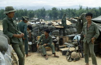 Vietnam War. Siege of Kontum. Montagnard soldiers gathered in base within a barbed wire perimeter. Young soldier sitting on a chair holding a medical syringe. Walls of sand bags  makeshift shelters  t...