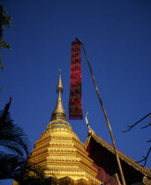 Wat Phran Tao.  Detail of pointed roof top of rare teak temple beside golden Chedi with red and gold prayer flag hanging in foreground. temple-monasterystupa Asian Prathet Thai Raja Anachakra Thai R...