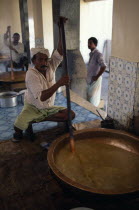 Men stirring large  shallow dish of halva.sweet confectionconfectionary Male Man Guy Middle East Omani Male Men Guy