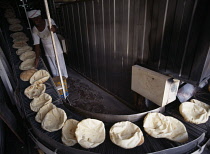 Bakery.  Arab bread on a conveyor belt after coming out of the oven.Cooking Arabic Middle East One individual Solo Lone Solitary Qatari