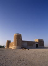 Exterior view of a fort with crenellated towers  built in 1938 and used as a police border post  now a museum.  A cannon in the foreground.   History Middle East Qatari