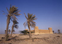 Exterior view of a fort with crenellated towers  built in 1938 and used as a police border post  now a museum.  Palm trees in the foreground.History Middle East Qatari