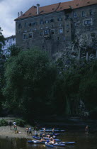 Czech Republic, South Bohemia, Cesky Krumlov, Canoeists relaxing on a river side with the Chateaux rising behind.