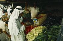 Man at vegetable stall in souk selling courgettes aubergines squash and tomatoes