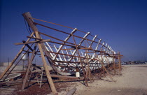 Traditional dhow boat building.  Man standing below wooden frame.Classic Classical Historical Male Men Guy Middle East Older One individual Solo Lone Solitary Qatari