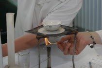 Teacher lighting a bunsen burner prior to it being used for a food technology experiment measuring the evaporation of a salt solution.European Immature Kids Learning Lessons Teaching