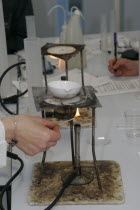 Teacher lighting a bunsen burner prior to it being used for a food technology experiment measuring the evaporation of a salt solution.European Immature Kids Learning Lessons Teaching