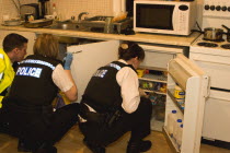 Police searching kitchen of residential home during drugs bust.European  European
