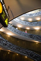 Vatican City Museums Tourists descending the Spiral Ramp designed by Giuseppe Momo in 1932 leading from the museums to the street level below seen from below with an illuminated sign warning to watch...